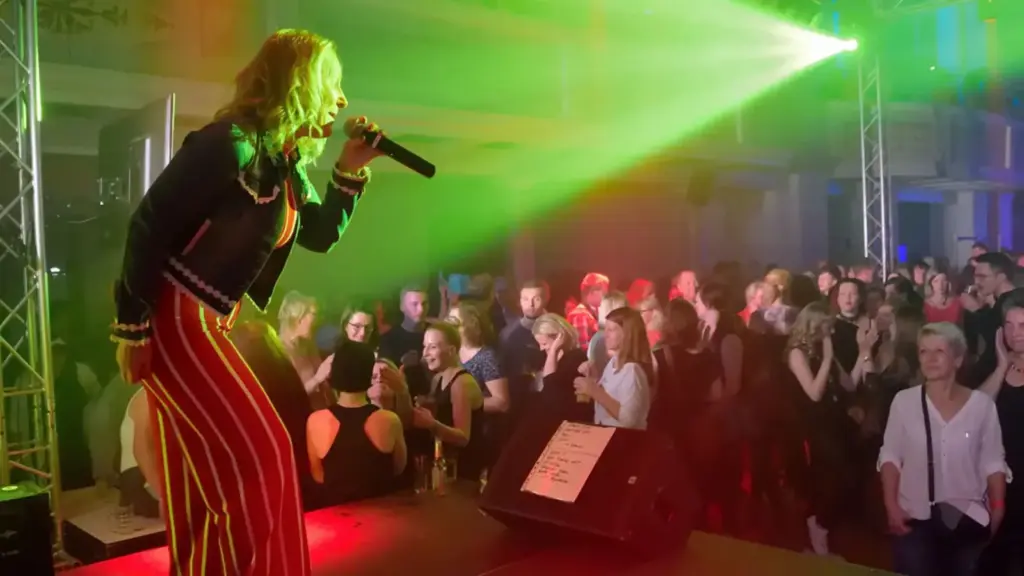 Corinna Anders auf der Bühne vor jubelndem Publikum unter buntem Bühnenlicht