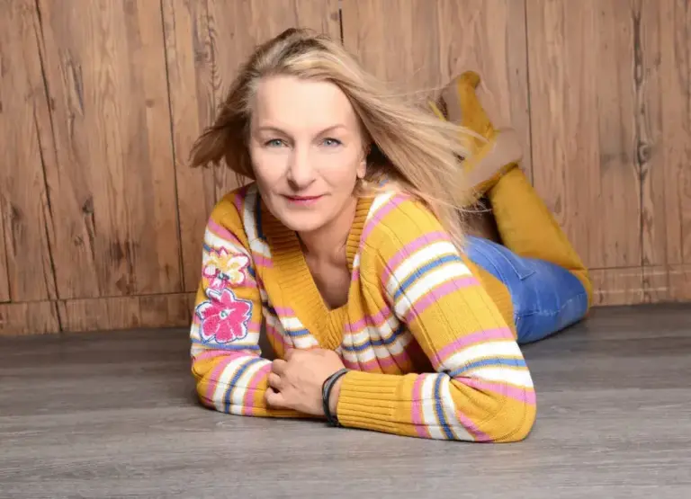 Corinna Anders liegt im gestreiften Pullover auf einem Holzboden und lächelt in die Kamera