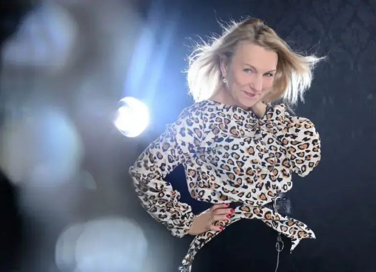 Corinna Anders lächelt in einer Bluse mit Leopardenmuster, helles Licht hinter ihr