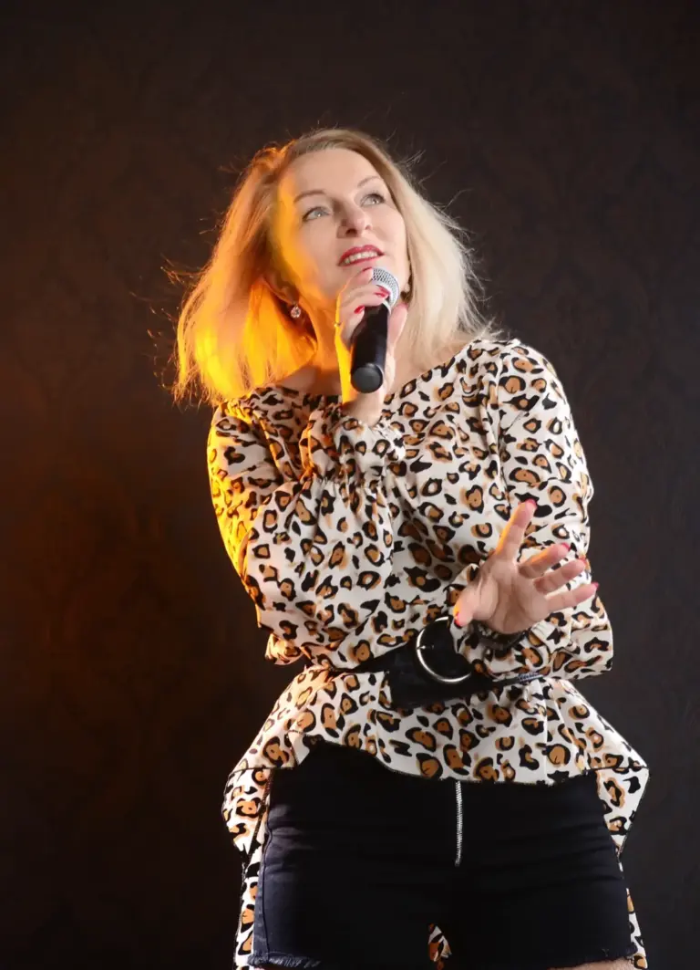Corinna Anders singt in einem Oberteil mit Leopardenmuster und schwarzen Shorts ins Mikrofon