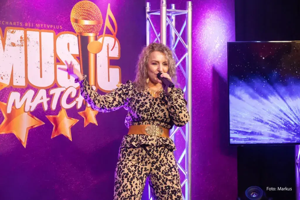 Corinna Anders im Outfit mit Leopardenmuster auf der Bühne von Music Match unter violetten Lichtern
