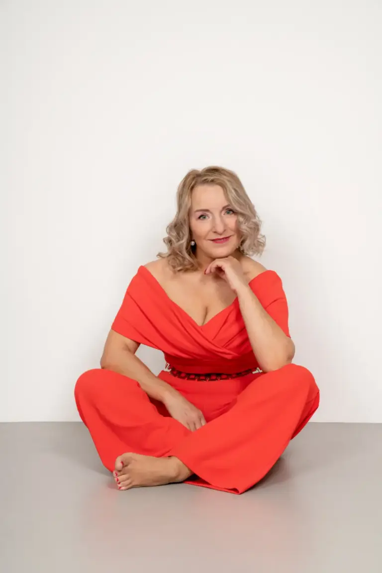 Corinna Anders im roten Outfit sitzt lächelnd vor weißem Hintergrund