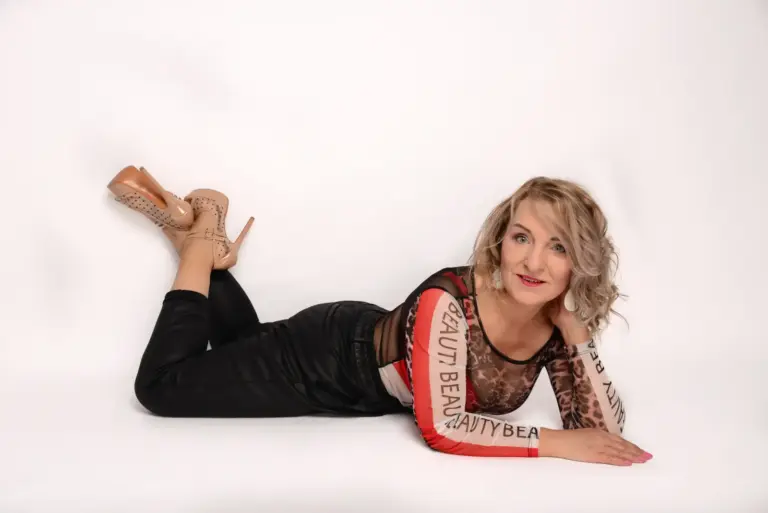 Corinna Anders liegt seitlich in schwarzer Hose und Heels auf weißem Untergrund
