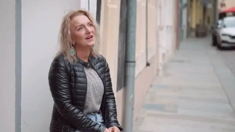 Corinna Anders sitzt in schwarzer Jacke an eine Mauer gelehnt und blickt nach oben