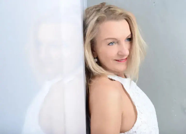 Corinna Anders lehnt im weißen Kleid an einer spiegelnden Wand